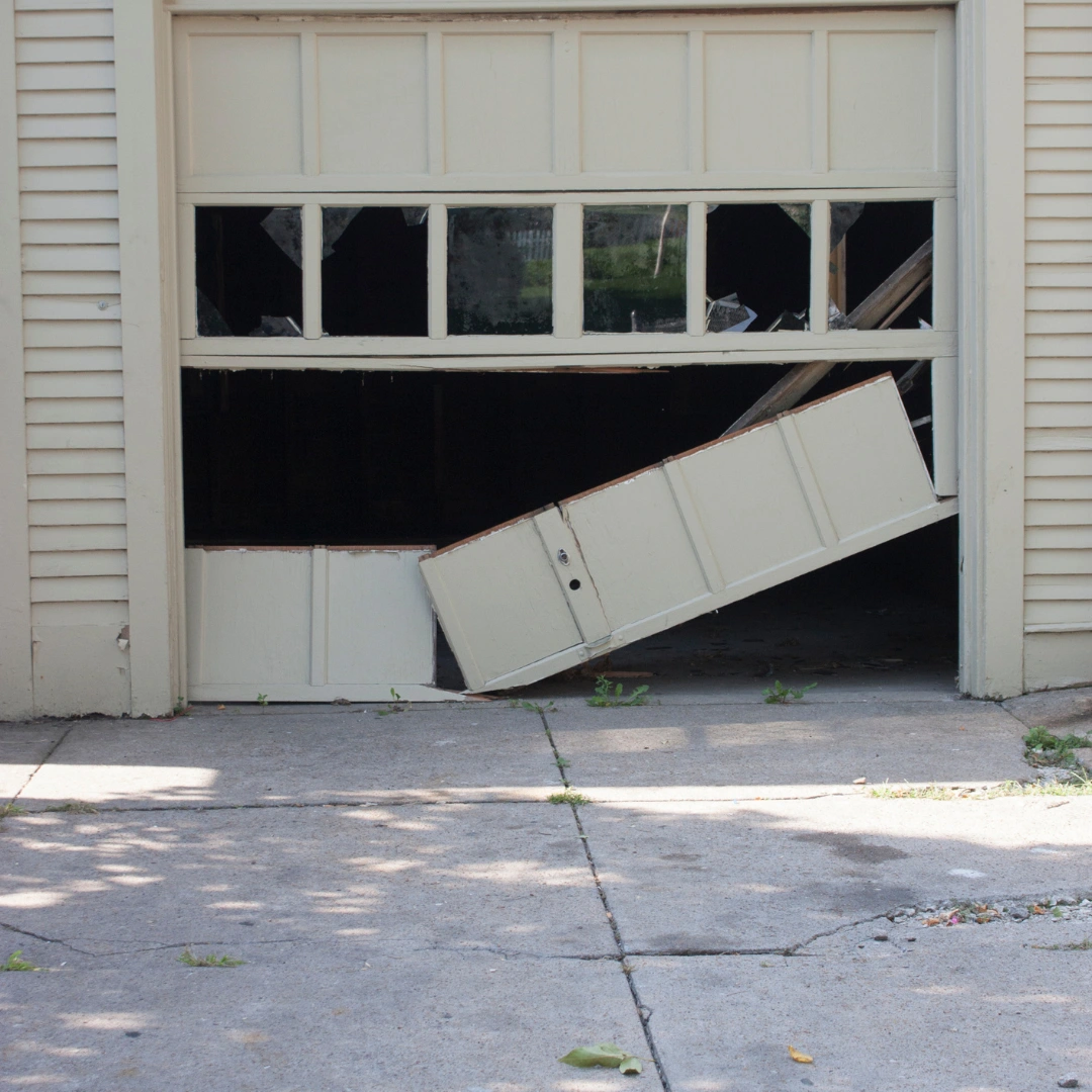 a broken white garage door and broken windows