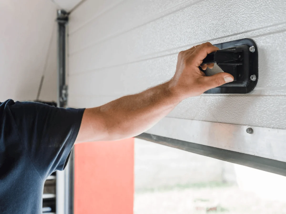 A man is opening a garage door with his hand