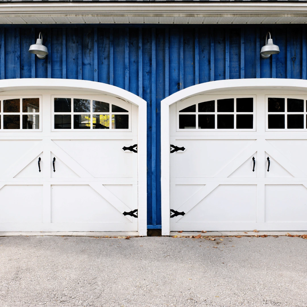 Two white ranch style garage doors in of a blue building